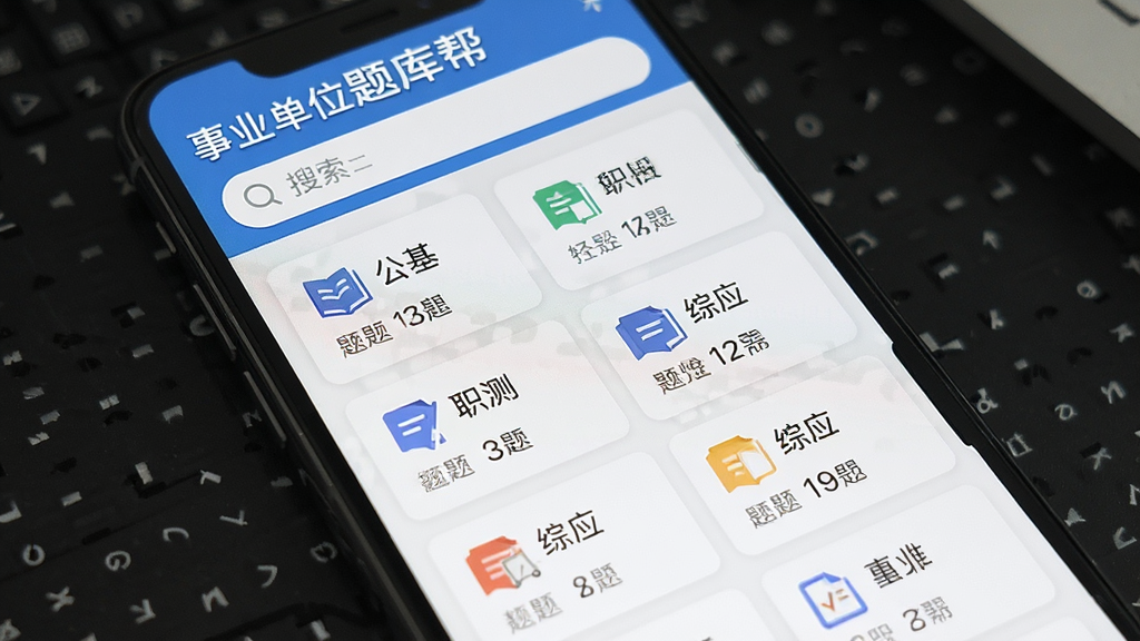 一张展示事业单位题库帮海量题库界面的图片,主体为手机屏幕显示分类列表,布局上方是搜索框,中间是公基、职测、综应等科目卡片,排版整齐,风格清爽简约,细节上每个科目卡片有对应图标和题目数量,画质干净、无多余元素,图片中文字包含“事业单位题库帮”