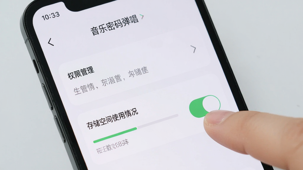 手机屏幕显示“音乐密码弹唱”的设置页面,页面中有权限管理选项和存储空间使用情况,旁边有手指正在点击开关按钮,背景是浅灰色,风格简洁明了,画质干净清晰