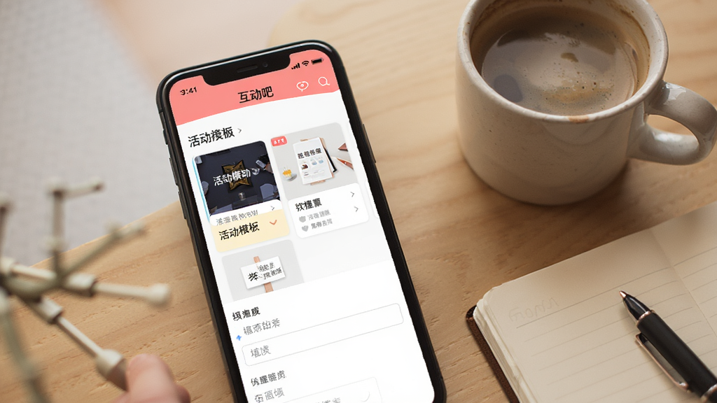 一张展示“互动吧”App发起活动页面的手机界面图,画面中有活动模板选择卡片和填写框,手机旁放着一杯咖啡和笔记本,风格温馨办公,画质清晰干净
