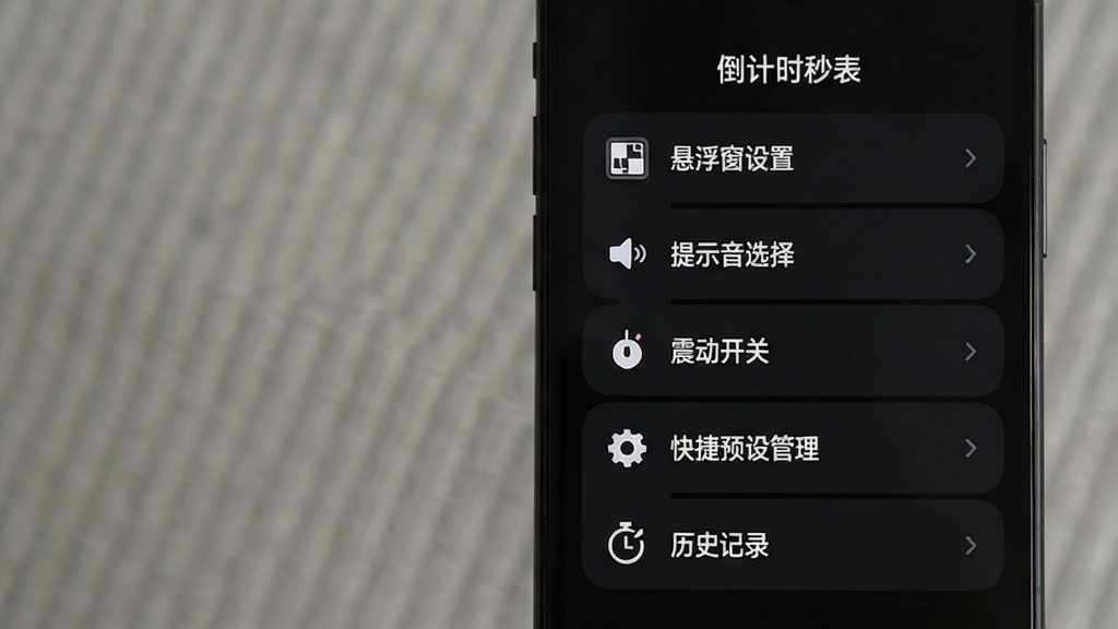 一张展示“倒计时秒表”应用设置菜单的图片,画面中手机屏幕显示深色主题界面,菜单从上到下依次列出“悬浮窗设置”“提示音选择”“震动开关”“快捷预设管理”“历史记录”等选项,每个选项旁边有简洁的图标。风格暗黑模式,文字清晰,布局整齐,画质干净无多余元素。