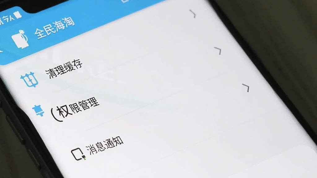 一部安卓手机屏幕显示“全民海淘”APP的设置界面,里面有清理缓存、权限管理、消息通知等选项,界面风格简洁,以白色和浅蓝色为主,文字清晰,无多余装饰
