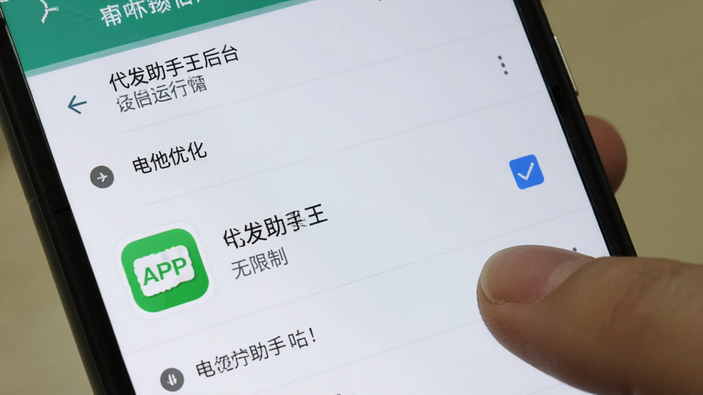 代发助手王后台运行设置界面,手机屏幕显示安卓系统的电池优化设置页面,代发助手王APP图标旁边有“无限制”选项被勾选,画面中有手指正在点击屏幕,背景是手机设置菜单的浅色界面,风格写实,画质清晰,文字指示明确,无多余装饰