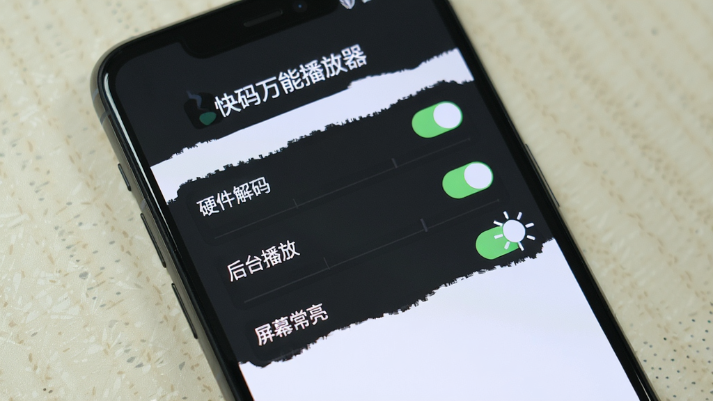 一张手机屏幕显示“快码万能播放器”的设置界面,上面有“硬件解码”、“后台播放”、“屏幕常亮”等开关选项,背景为浅色桌面,整体风格简洁,画质清晰,无多余元素。