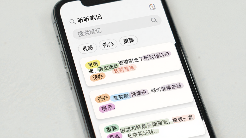 主体:手机屏幕显示“听听笔记”的笔记列表,段落被不同颜色标签标记,顶部有搜索框;布局:手机竖向放置,屏幕内从上到下依次是搜索框、标签筛选栏、三条笔记卡片;排版:标签有“灵感”“待办”“重要”等字样,文字清晰;风格:扁平化UI设计,色彩柔和;细节:搜索框内有放大镜图标,笔记卡片有浅色阴影;画质:高清屏幕截图风格,干净无多余元素。