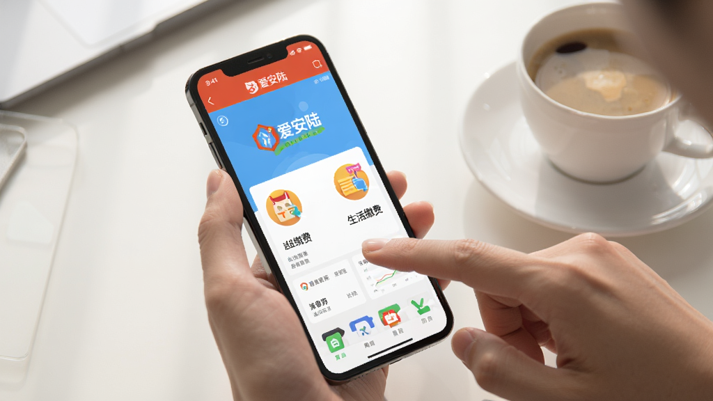 图片描述:一张清晰的智能手机使用场景图,手机屏幕显示“爱安陆”应用的主页,手指正点击“生活缴费”图标,背景是简洁的桌面,旁边放着一杯咖啡,整体画风自然明亮,细节真实,突出用户正在操作应用的场景,画质干净,无多余元素。
