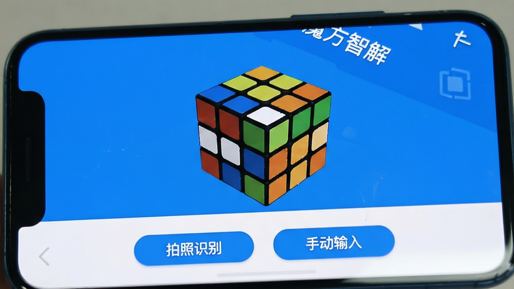 一张手机屏幕的特写,屏幕中显示“魔方智解”主界面,界面为简洁的蓝白风格,中央是一个虚拟的3D魔方模型,下方有“拍照识别”和“手动输入”两个按钮,界面干净,画质清晰,无多余元素。