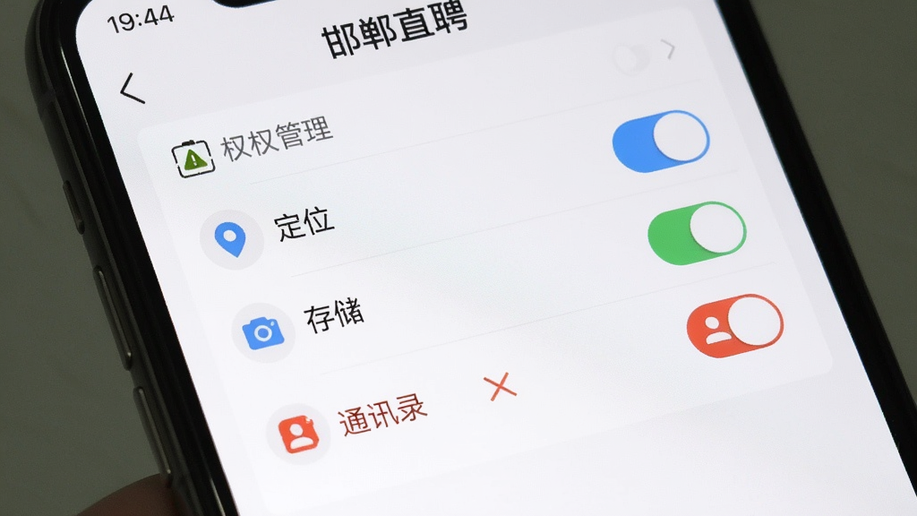 生图提示词:手机屏幕截图,展示“邯郸直聘”APP的权限管理界面,画面中有“定位”“存储”“相机”等权限开关,其中“通讯录”权限被标红并打叉,界面风格清晰明了,带有安全提示图标,画质干净