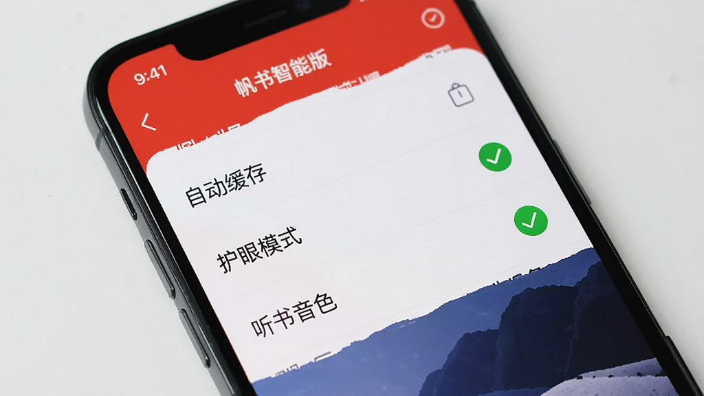 一部手机展示着帆书智能版的设置菜单界面,菜单项包括“自动缓存”、“护眼模式”、“听书音色”等,旁边有一个绿色的对勾图标,画面风格简洁明快,背景是浅灰色,画质干净无多余元素