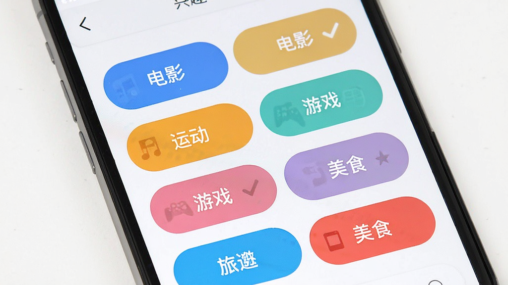 全球热恋 兴趣标签选择界面 手机屏幕显示多个彩色标签按钮 如音乐 电影 运动 游戏 旅行 美食 标签有选中和未选中状态 背景是白色 风格清新活泼 画质干净 无多余元素