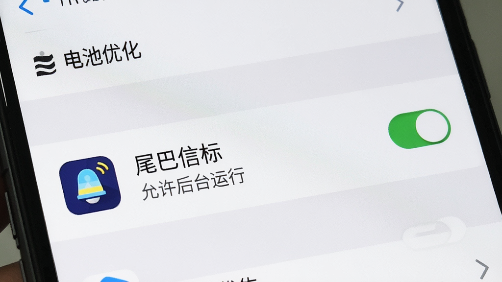一张展示手机电池优化设置界面的图片,屏幕内显示应用列表中有“尾巴信标”的图标和名称,旁边有“允许后台运行”的开关按钮处于开启状态,屏幕上方有“电池优化”的标题,整体风格为系统原生设置界面风格,色调以白色和浅灰为主,画质清晰,无多余元素