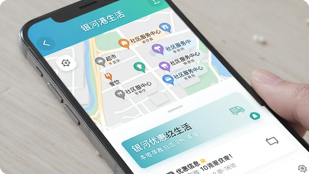 银河港生活APP本地资讯页面,手机屏幕显示地图模式,地图上标注了周边超市、餐饮、社区服务中心等位置点,下方列表展示具体优惠信息,界面以蓝绿色为主色调,风格清新,画质干净无多余元素
