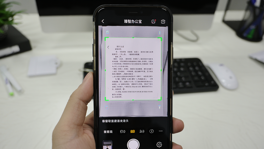 手机拍摄纸质文档,屏幕上显示“臻智办公宝”的扫描界面,文档边缘被绿色框自动识别,下方出现提取出的文字内容,背景是办公桌,风格写实,画质清晰,无多余元素