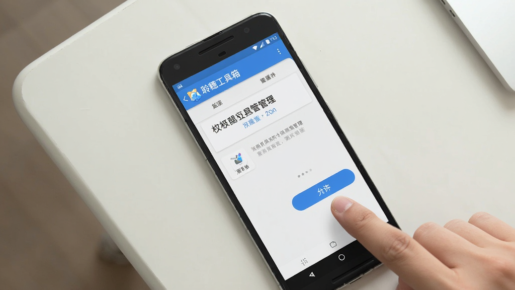 一张手机操作示意图,画面以俯视角度展示一部安卓手机放在桌面上,屏幕上显示“聆穗工具箱”的权限管理界面,旁边有一只手指正在点击“允许”按钮,背景是简洁的浅色桌面,光线明亮柔和,画面风格写实清晰,画质干净,无多余元素