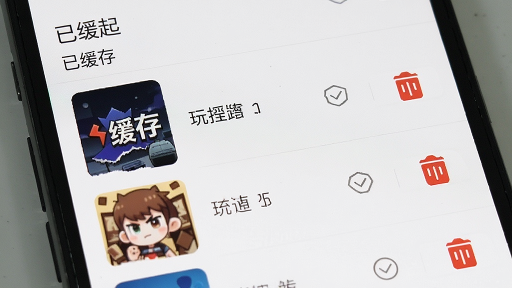 手机屏幕显示“玩得起”App的下载缓存管理界面,列表中有多个已缓存的内容,每个条目旁边有删除按钮,顶部有“已缓存”标题,界面风格简洁,画质干净无多余元素