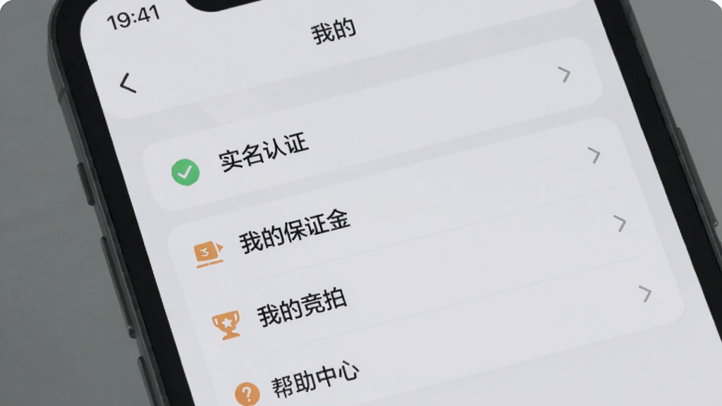 一部手机屏幕显示优信拍APP的“我的”页面,页面上有“实名认证”“我的保证金”“我的竞拍”“帮助中心”等选项,背景是简洁的浅灰色,主体是手机和功能菜单,布局清晰,风格扁平化,细节圆润,画质干净无多余元素
