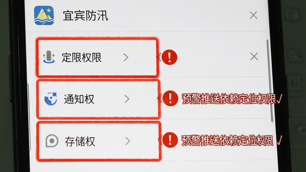 宜宾防汛权限设置引导界面,手机屏幕显示应用权限管理页面,定位权限、通知权限、存储权限三项被高亮标注,旁边有红色感叹号提示“预警推送依赖定位权限”,顶部标注“宜宾防汛”应用名称,背景为安卓系统设置页面,风格清晰直观,画质干净无多余元素