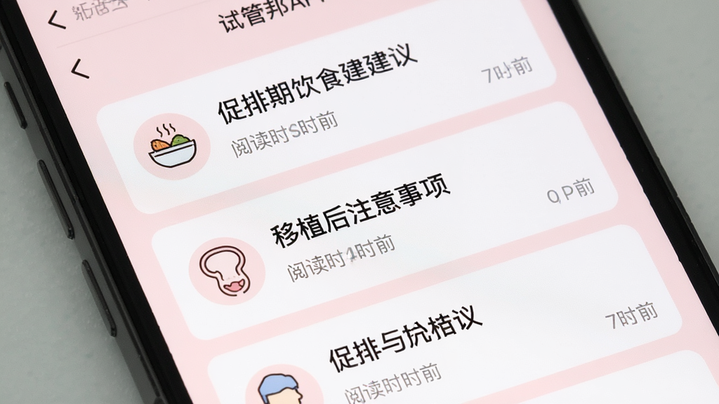 试管邦APP的知识库页面,手机屏幕显示着文章列表,标题包括“促排期饮食建议”“移植后注意事项”等,每篇文章配有简洁的图标和阅读时长,整体排版干净,字体适中,背景为柔和的浅粉色,画质清晰,无多余元素